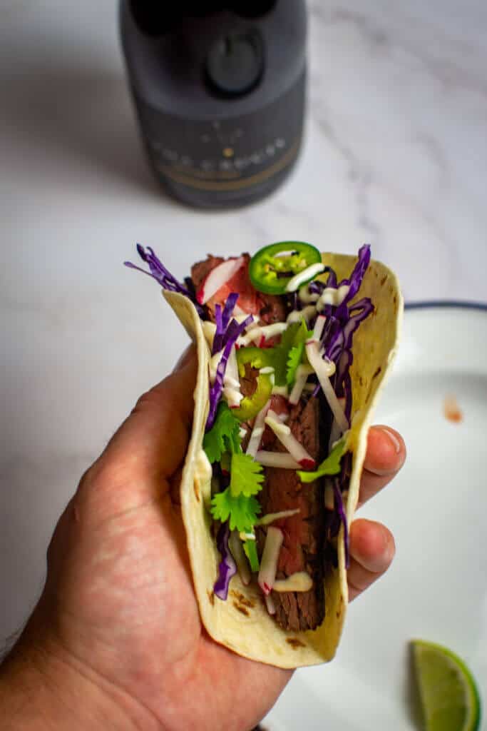 someone holding a steak taco carne asada style with a chalk hill alpha crucis grenache wine in backgrounde with a chalk hill alpha crucis grenache wine in background