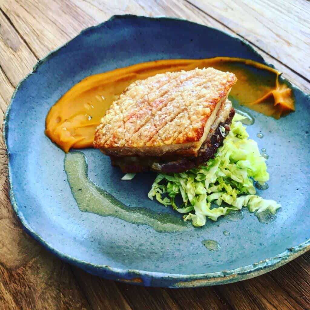 Crispy pork belly, sweet potato puree, cabbage & cider sauce on a plate