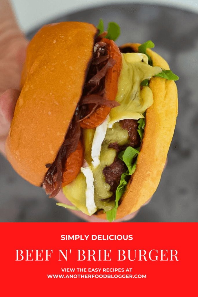 someone holding an organic beef burger with brie, roasted tomatoes & onion marmalade