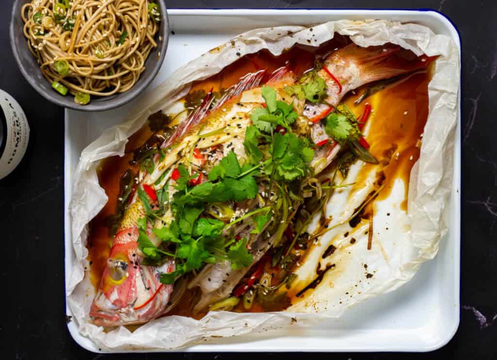 Cooked fish en papillote with bowl of noodles
