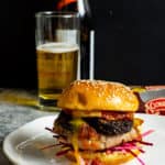 Pork & black pudding burger on a white plate with a beer in background