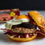 Pork & black pudding burger on a white plate with top bun off. Clonakilty pudding packet in background