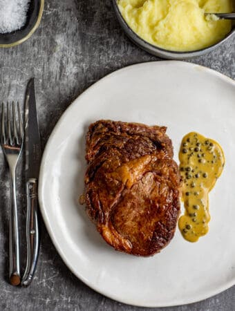 Rib fillet, pepper sauce, mashed potatoes and cutlery on a table