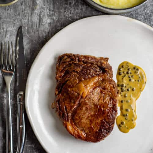 Rib fillet, pepper sauce, mashed potatoes and cutlery on a table