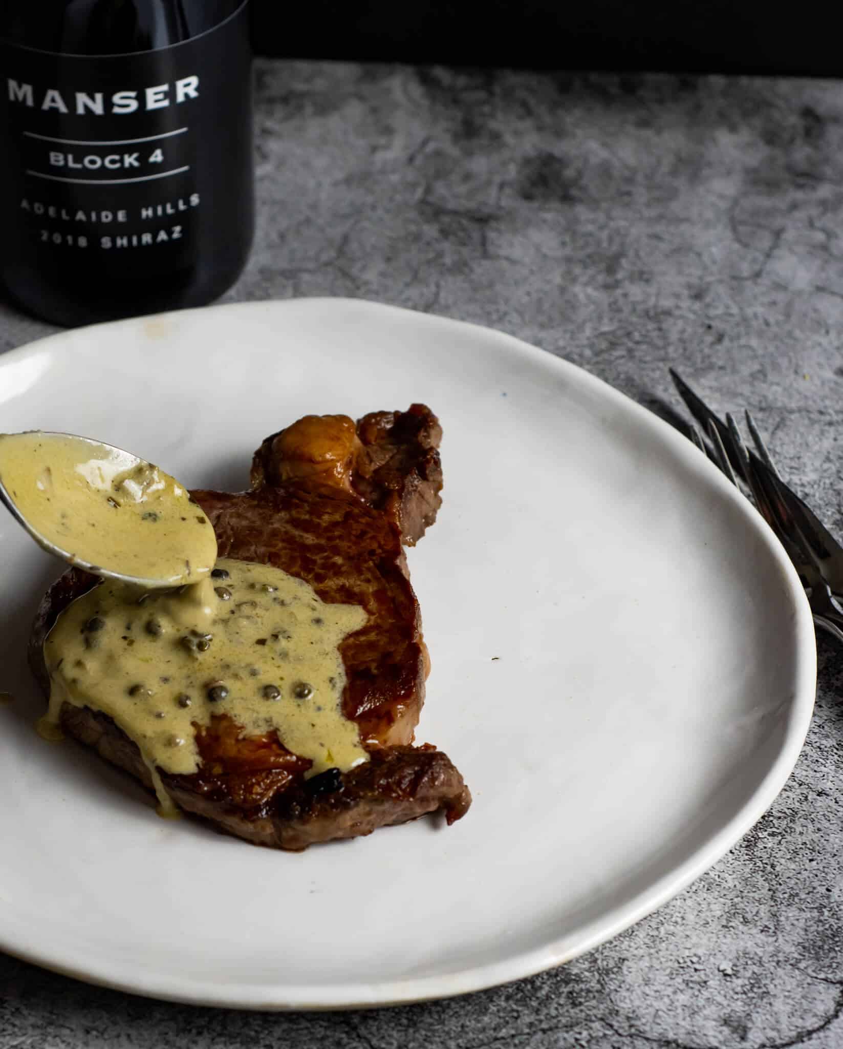 peppercorn sauce being spooned over steak & manser red wine