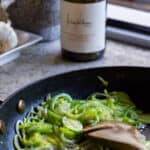 leeks cooking in a pan with a wine bottle in background