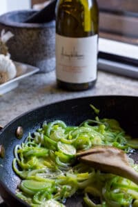 leeks cooking in a pan with a wine bottle in background