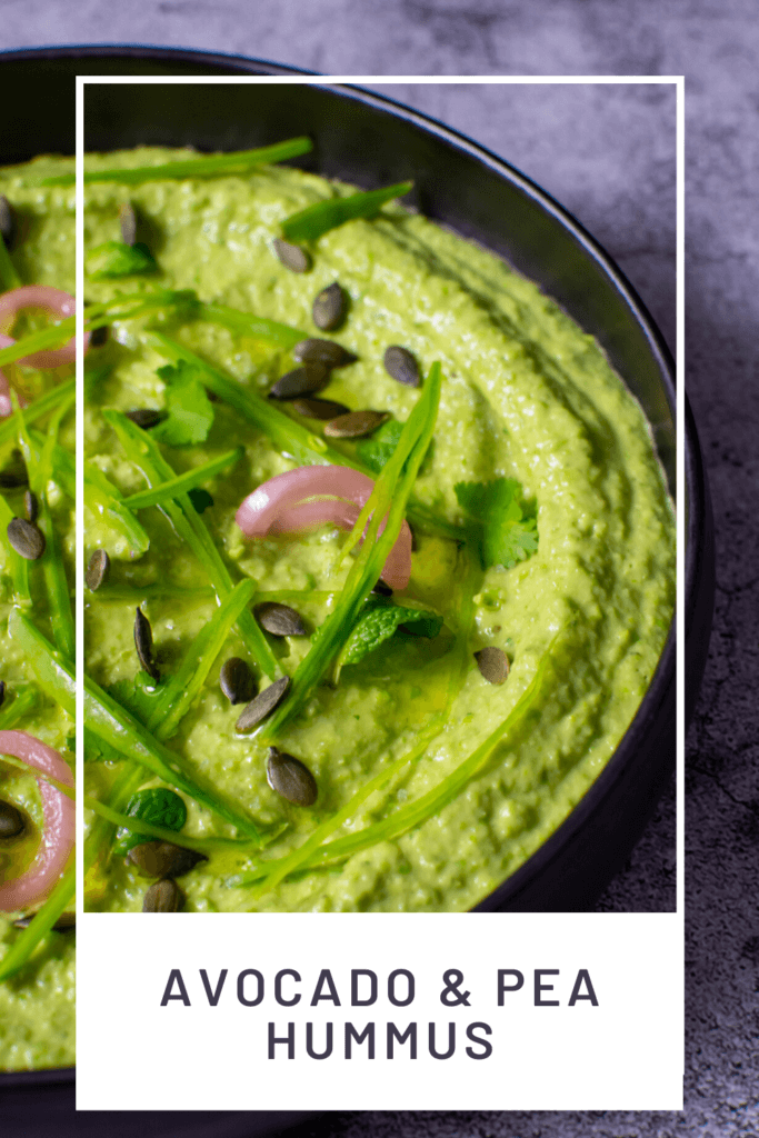 black bowl with avocado & pea hummus topped with pickled onions, pepitas, herbs & snowpeas