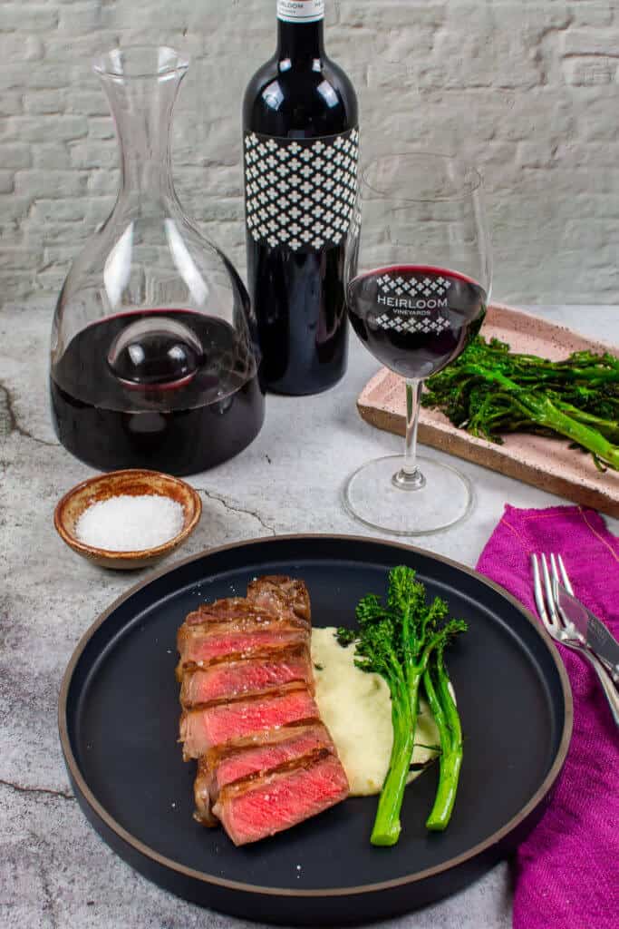 steak & onion soubise on a plate, decanter, glass of wine and bottle heirloom shiraz