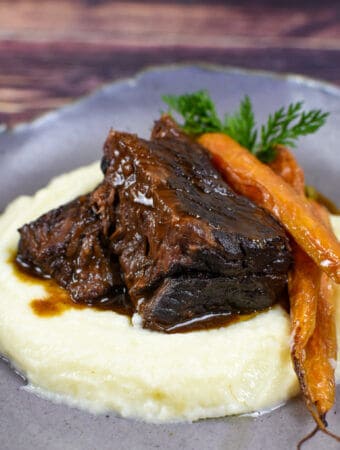 mushroom braised short ribs, cauliflower puree & carrots in a bowl on wooden table