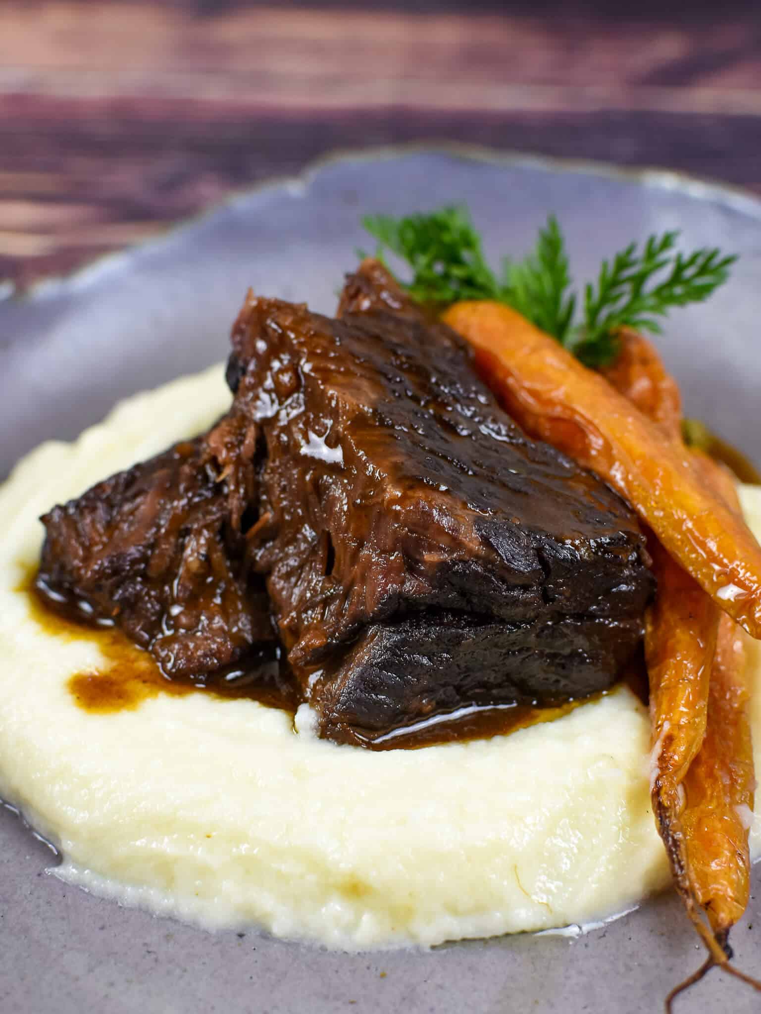 mushroom braised short ribs, cauliflower puree & carrots in a bowl on wooden table