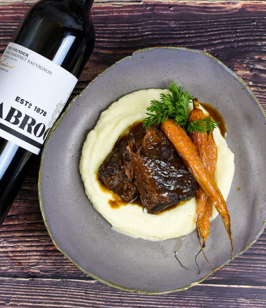 seabrook cabernet sauvignon, braised short ribs, cauliflower puree & carrots on a plate