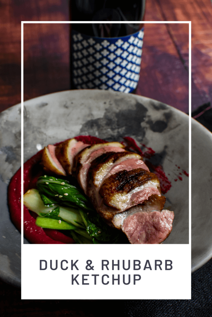Duck breast, rhubarb ketchup & asian greens in a made of australia bowl on a table with heirloom pinot noir