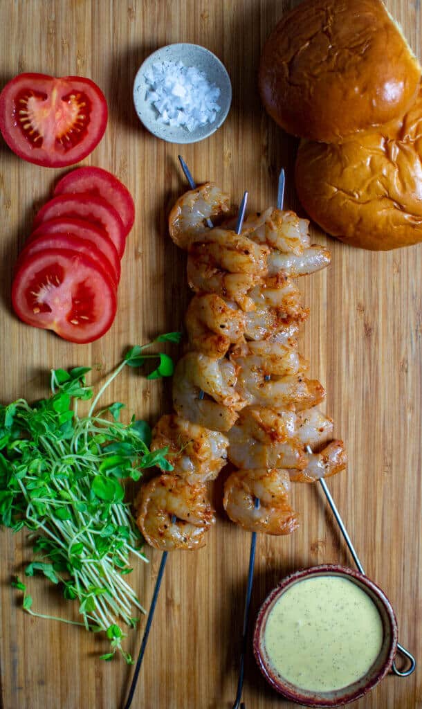 marinated prawn skewers, tomatoes. peashoots & brioche buns on a chopping board