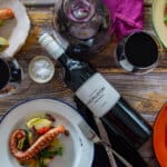 birds eye view of grilled octopus salad, wine glasses, cutlery and bottle of heirloom wine