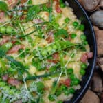 pea & bacon risotto in a black bowl on top of loads of stones