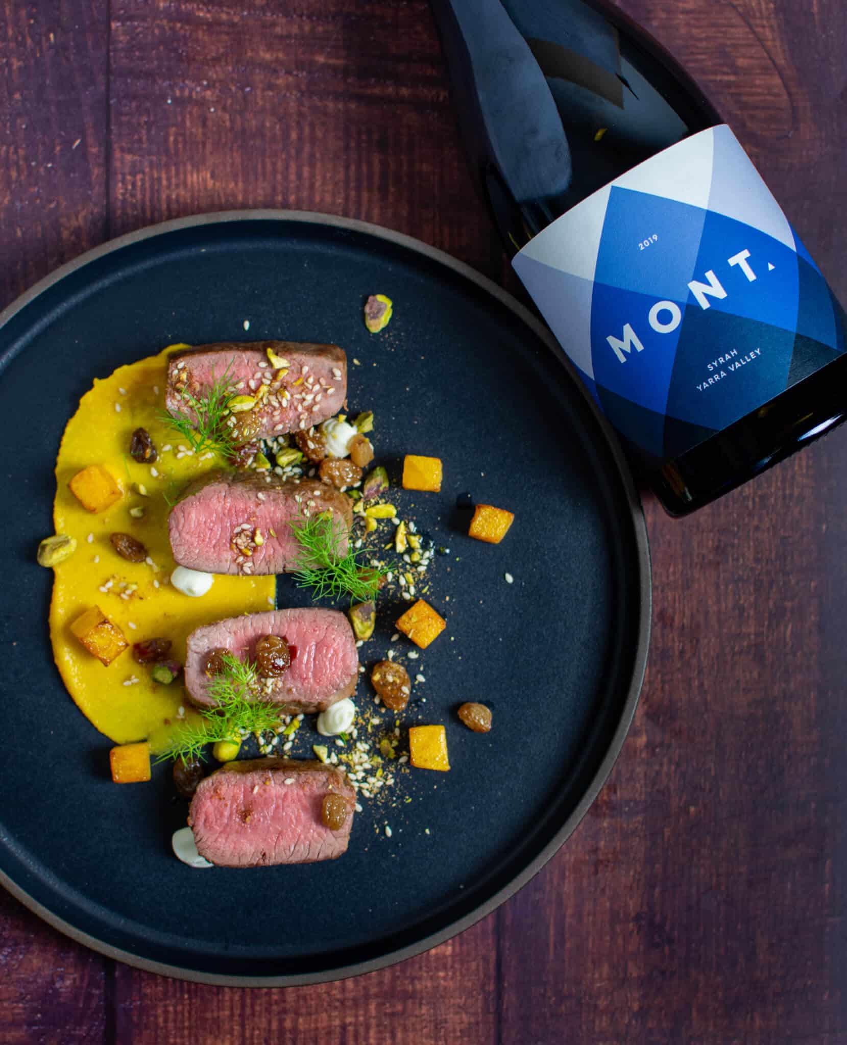 lamb, smoked squash puree, & pistachio dukkah on a black plate with mont wines syrah next to it