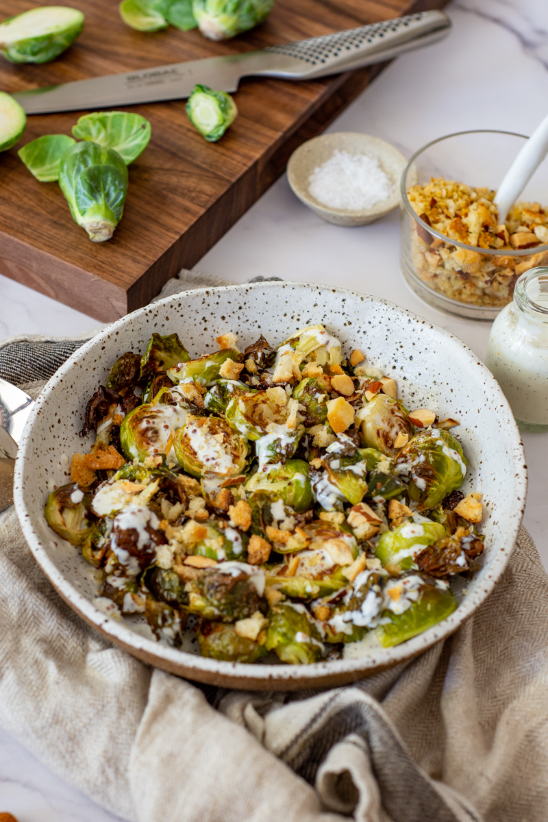 charred brussel sprouts & pangrattato in a bowl with a chopping board, brussel sprouts in the background