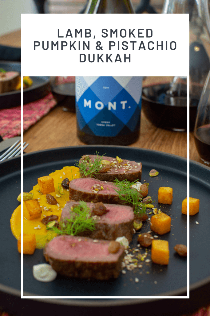 lamb, smoked squash puree, & pistachio dukkah on a black plate with mont wines syrah & wine glasses next to it