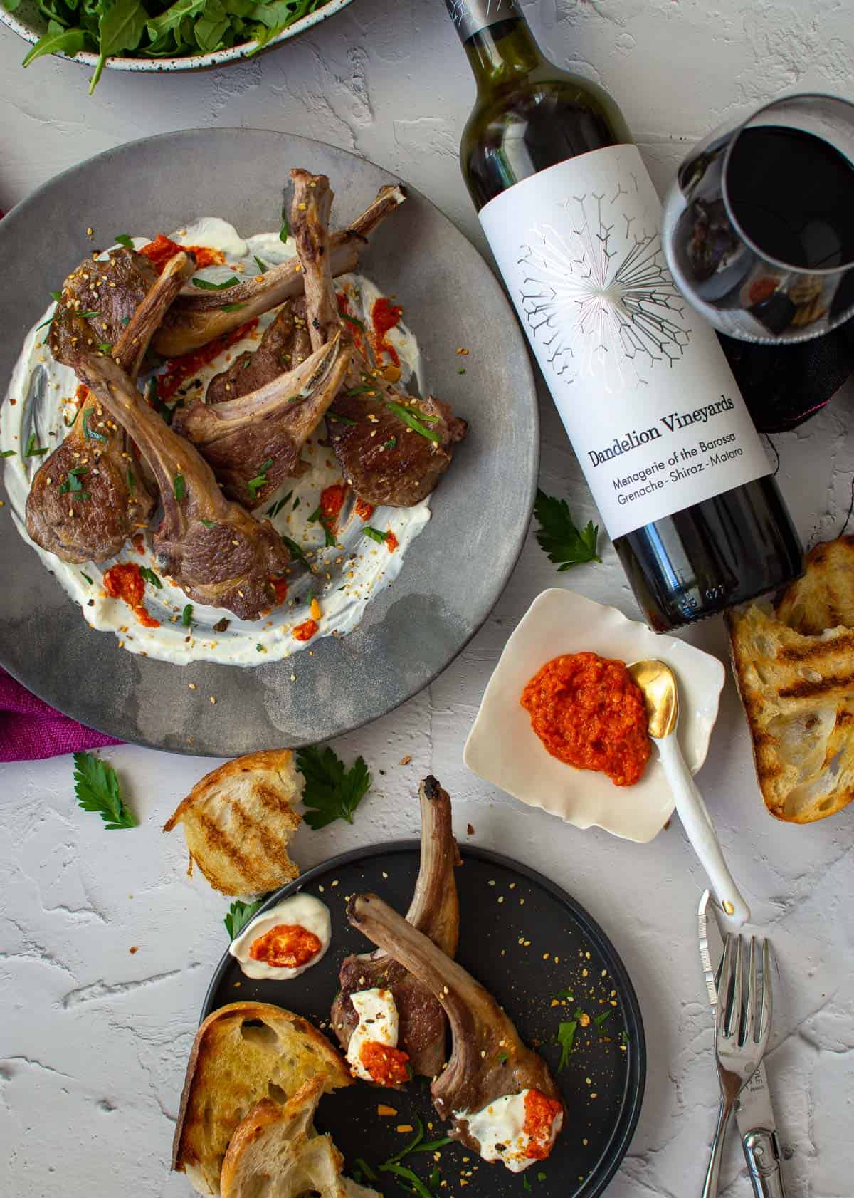 dandelion gsm wine, grilled bread and grilled lamb chops on a plate with harissa and labneh