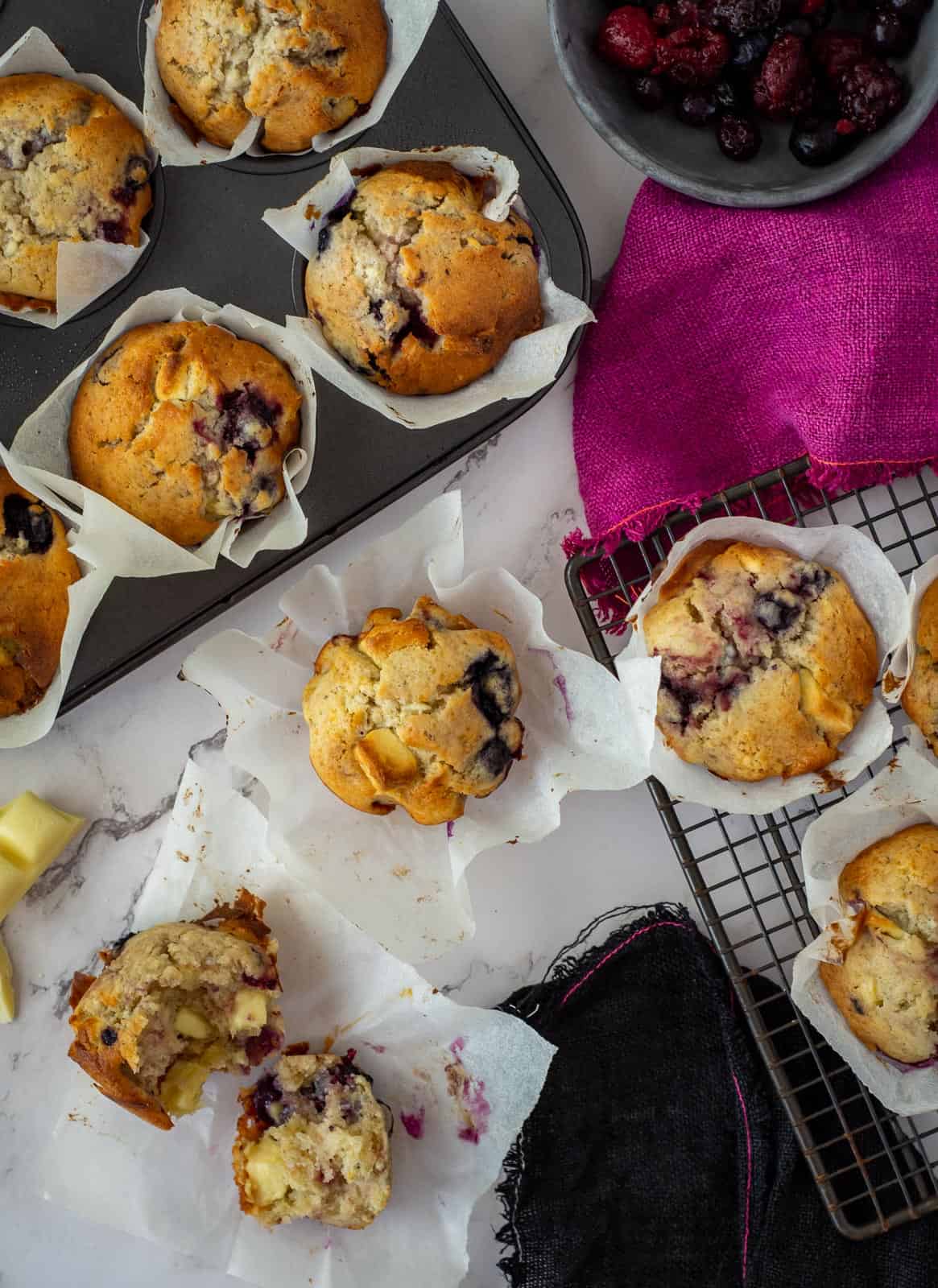 white chocolate muffins on countertop, some on a wire rack and in a muffin tray