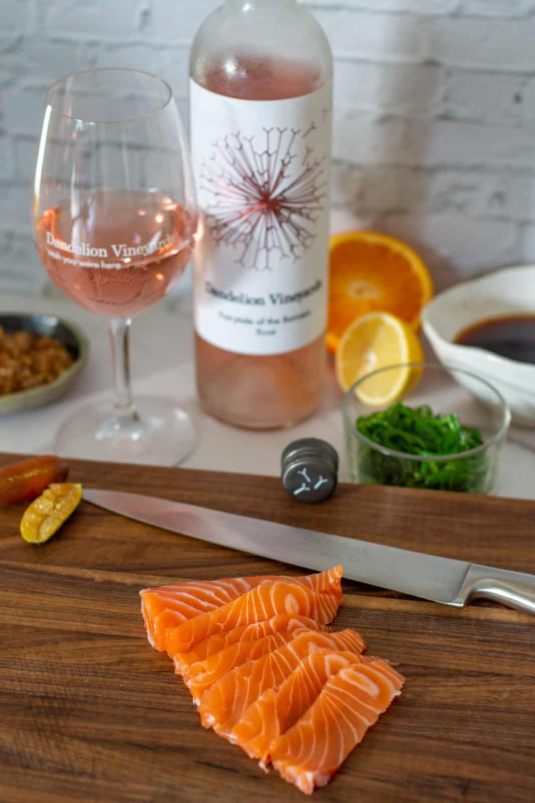 sliced raw salmon on a chopping board, dandelion rose & ponzu sauce ingredients in background