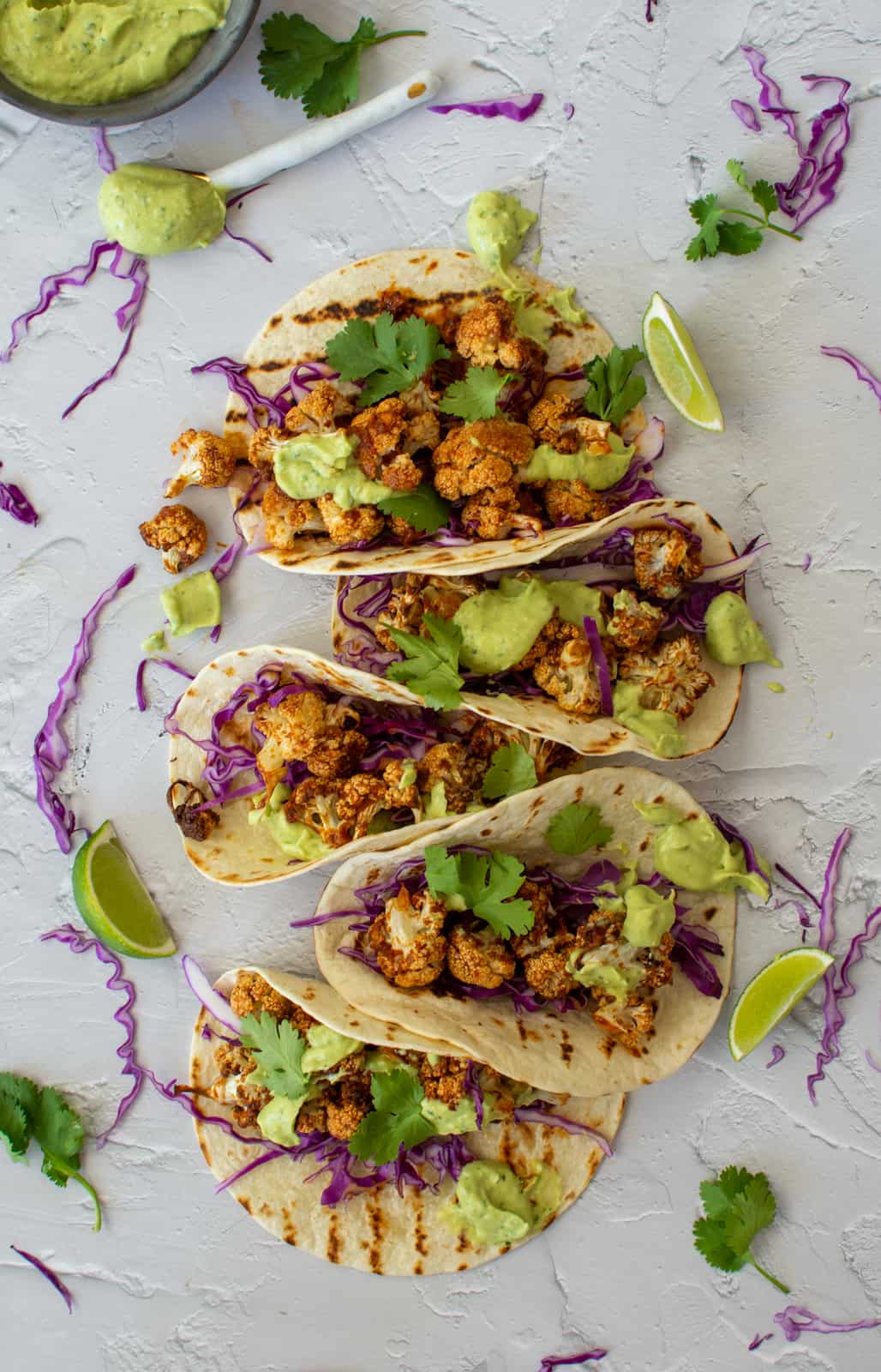 5 grilled cauliflower tacos on a counter top with lime and red cabbage sprinkled around them