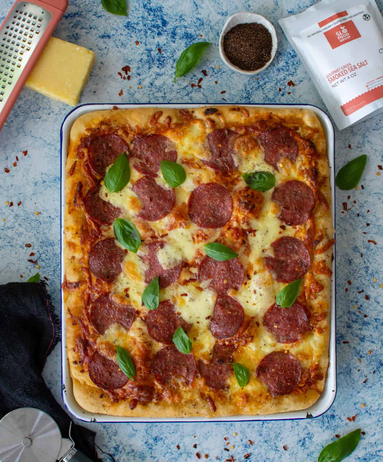 baking tray pizza (aka focaccia pizza) in a tray with parmesan cheese and smoked sea salt next to it