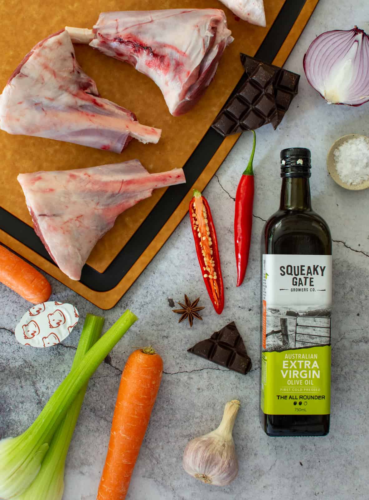 lamb shanks on a chopping board, squeaky gate olive oil and vegetables next to them