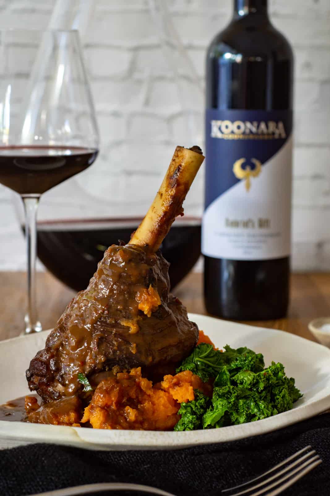 chilli & chocolate braised lamb shanks on a white plate with koonara cabernet sauvignon in background