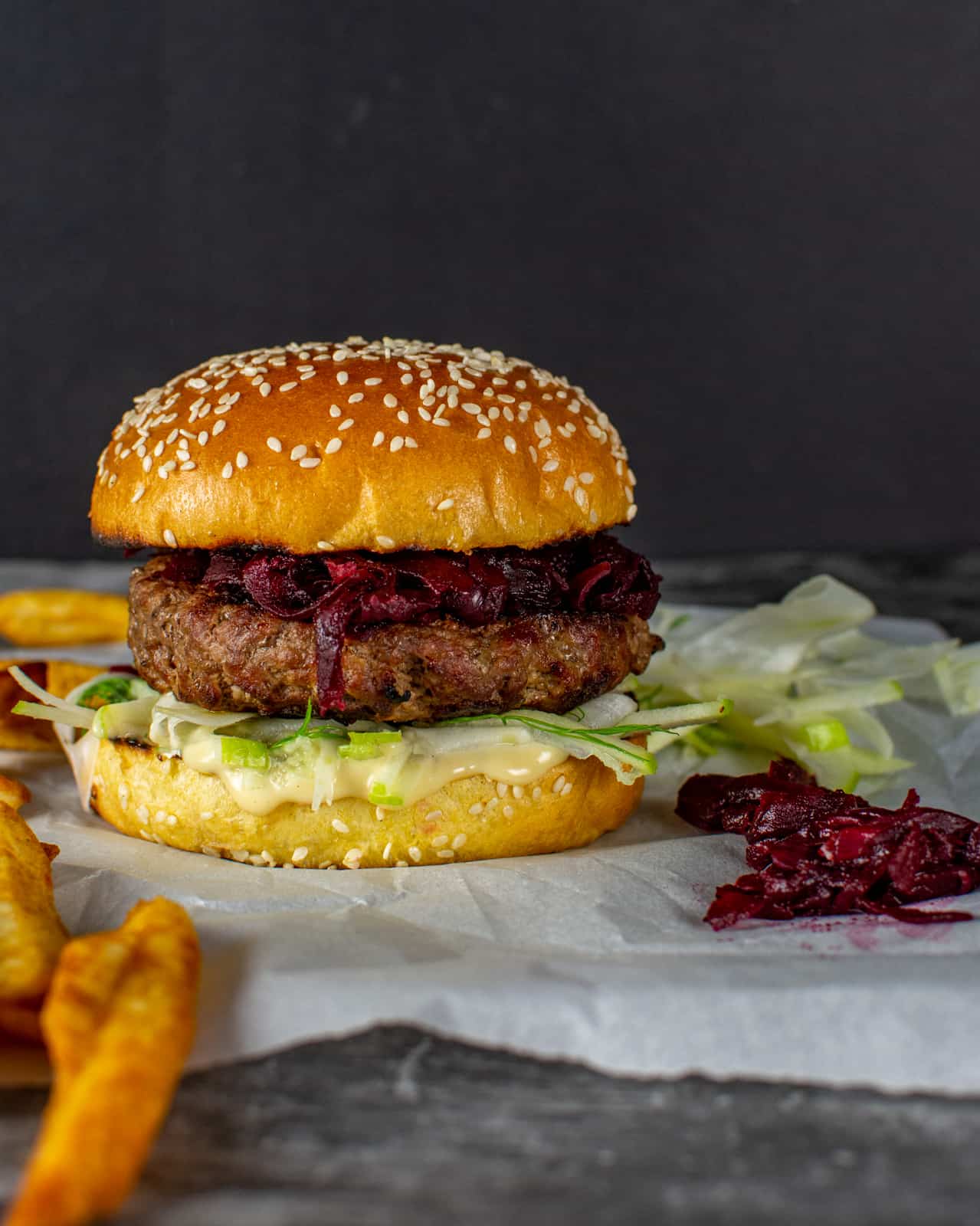 beef burger, apple/fennel slaw, garlic mayo and beetroot relish on parchment paper with chips next to it