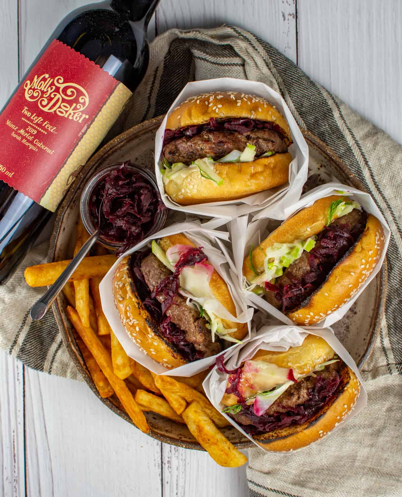 4 Aussie 'style' Burgers in a bowl with chips and relish on side. Bottle of red wine next to them