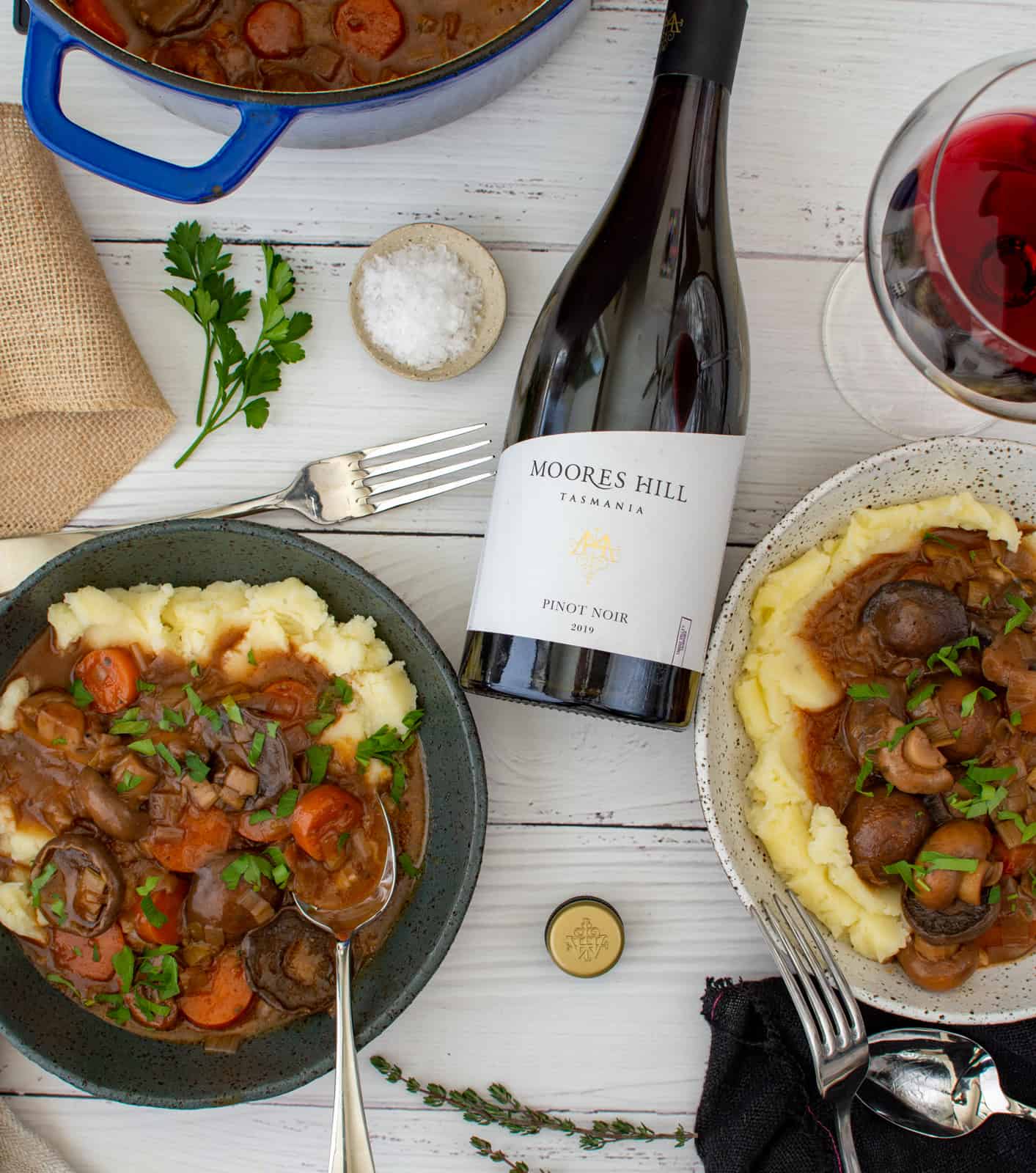 two bowls of stew on a table with glass of wine, bottle of wine and pot of stew beside them