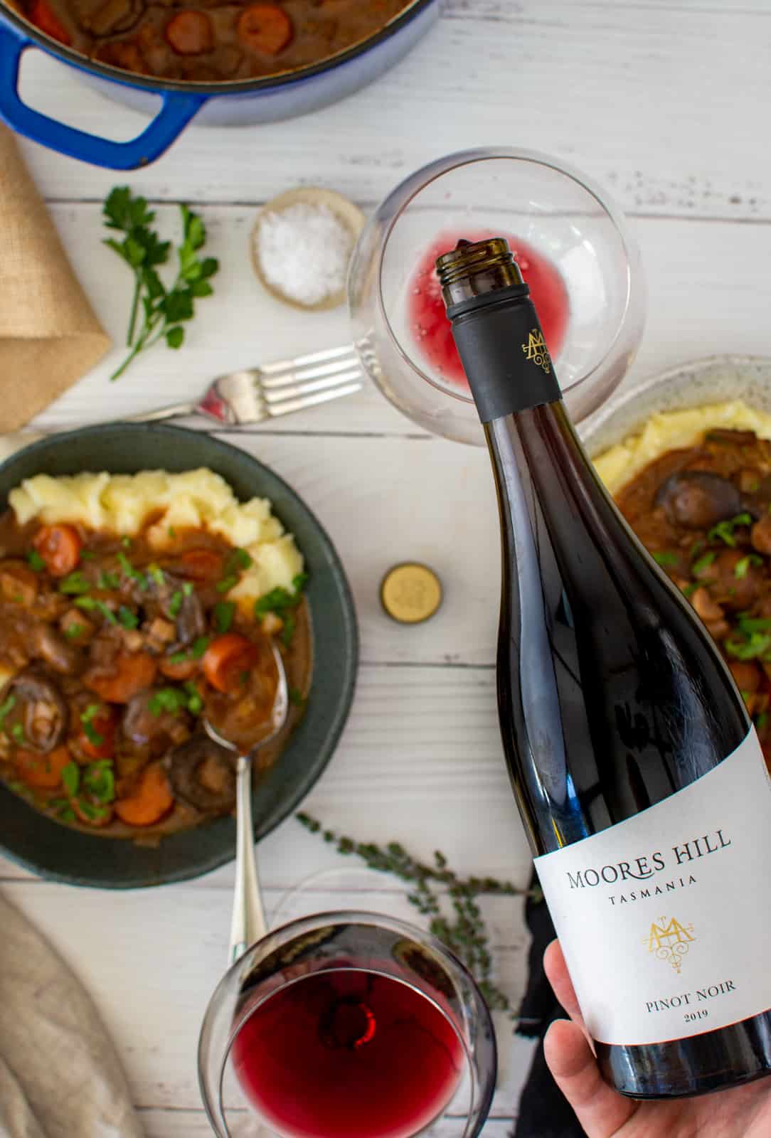 moores hill pinot noir being poured, bowls of stew on a white table beneath