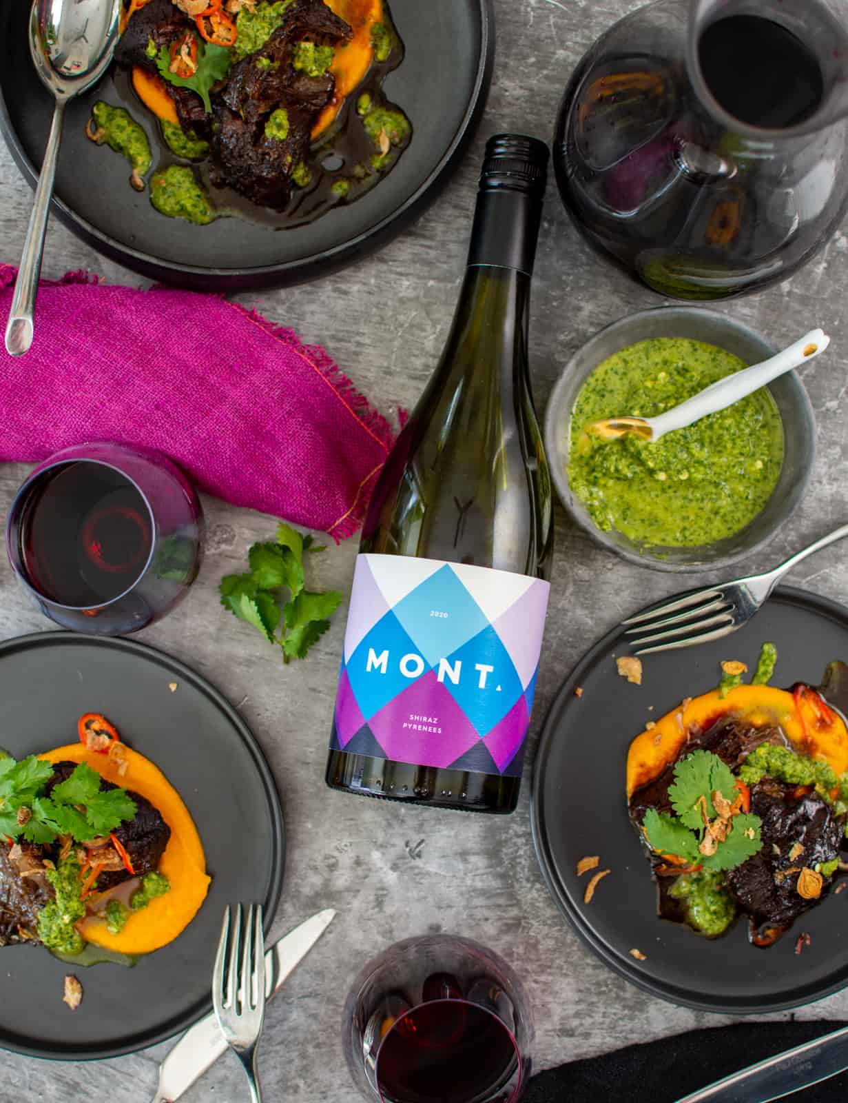 asian slow cooked beef cheeks in black plates, mont shiraz wine bottle