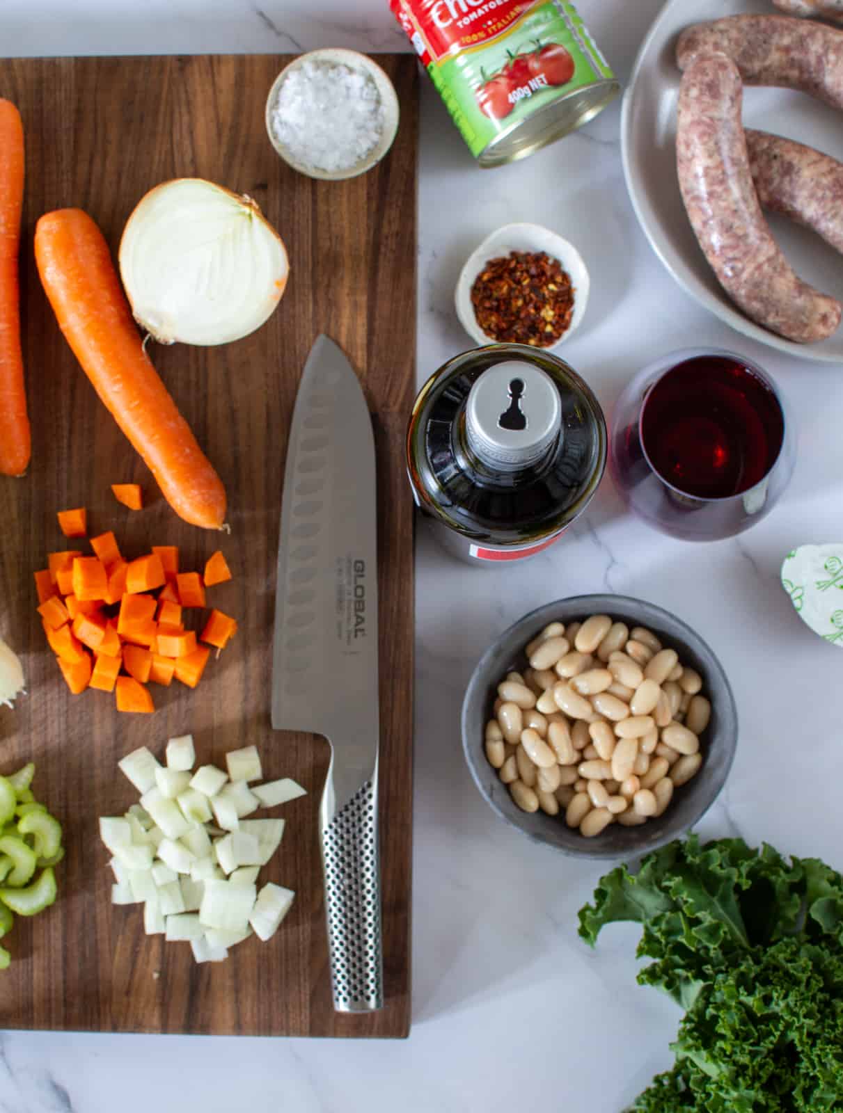 ingredients to make italian sausage stew on chopping board and chef knives, bottle of wine beside