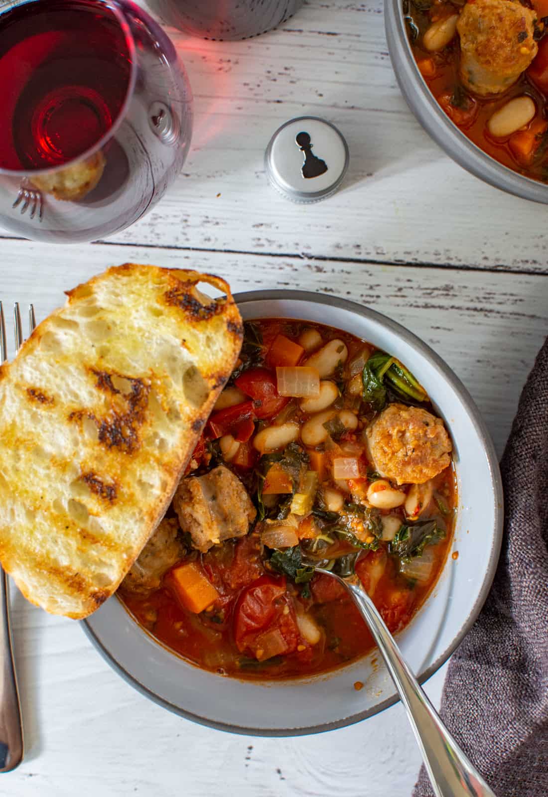 bowl of tuscan sausage stew, red wine and pawn wine co bottle cap