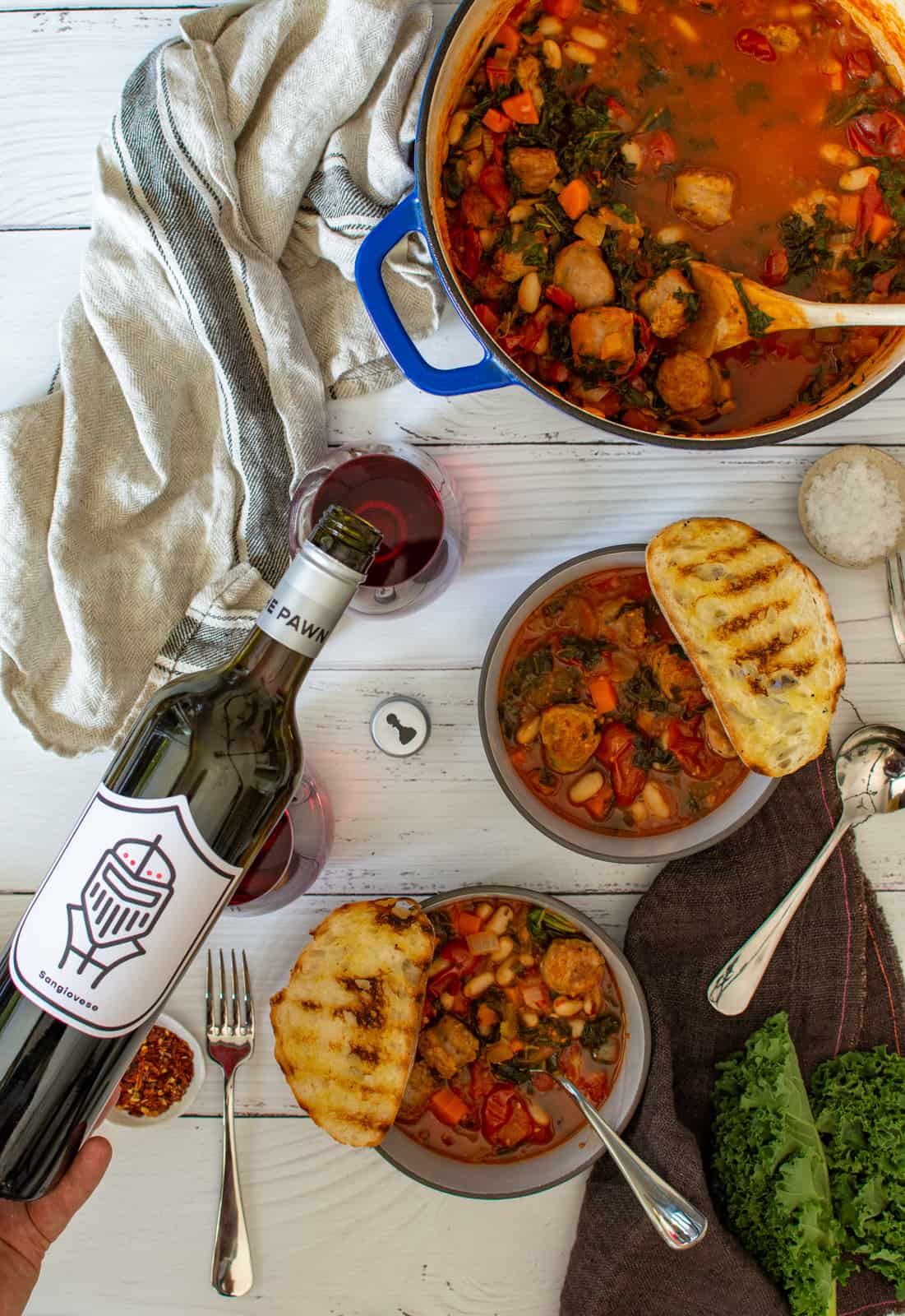 bowls of tuscan sausage stew on table with napkins and someone pouring pawn wine co sangiovese wine