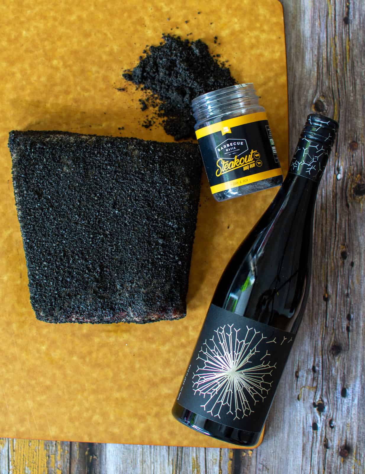 beef ribs rubbed in barbecue mafia rub on chopping board and a bottle of dandelion wine