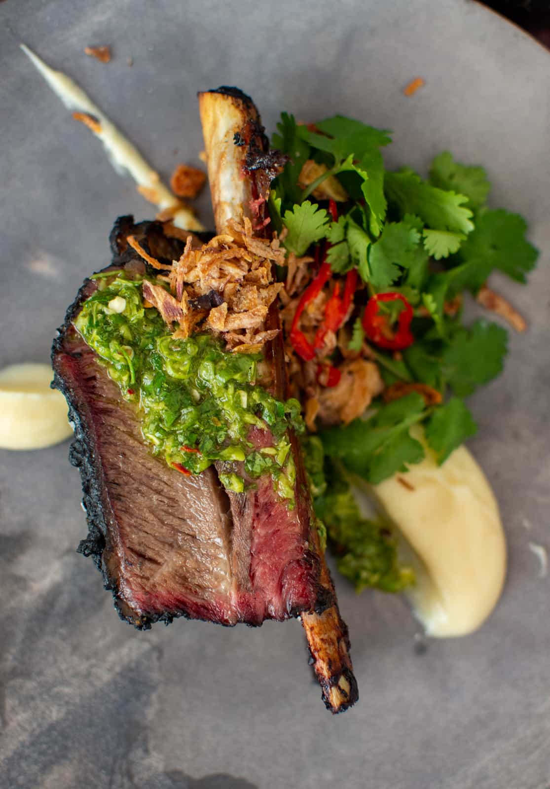 smoked short rib on a grey plate with cauliflower puree and chimichurri