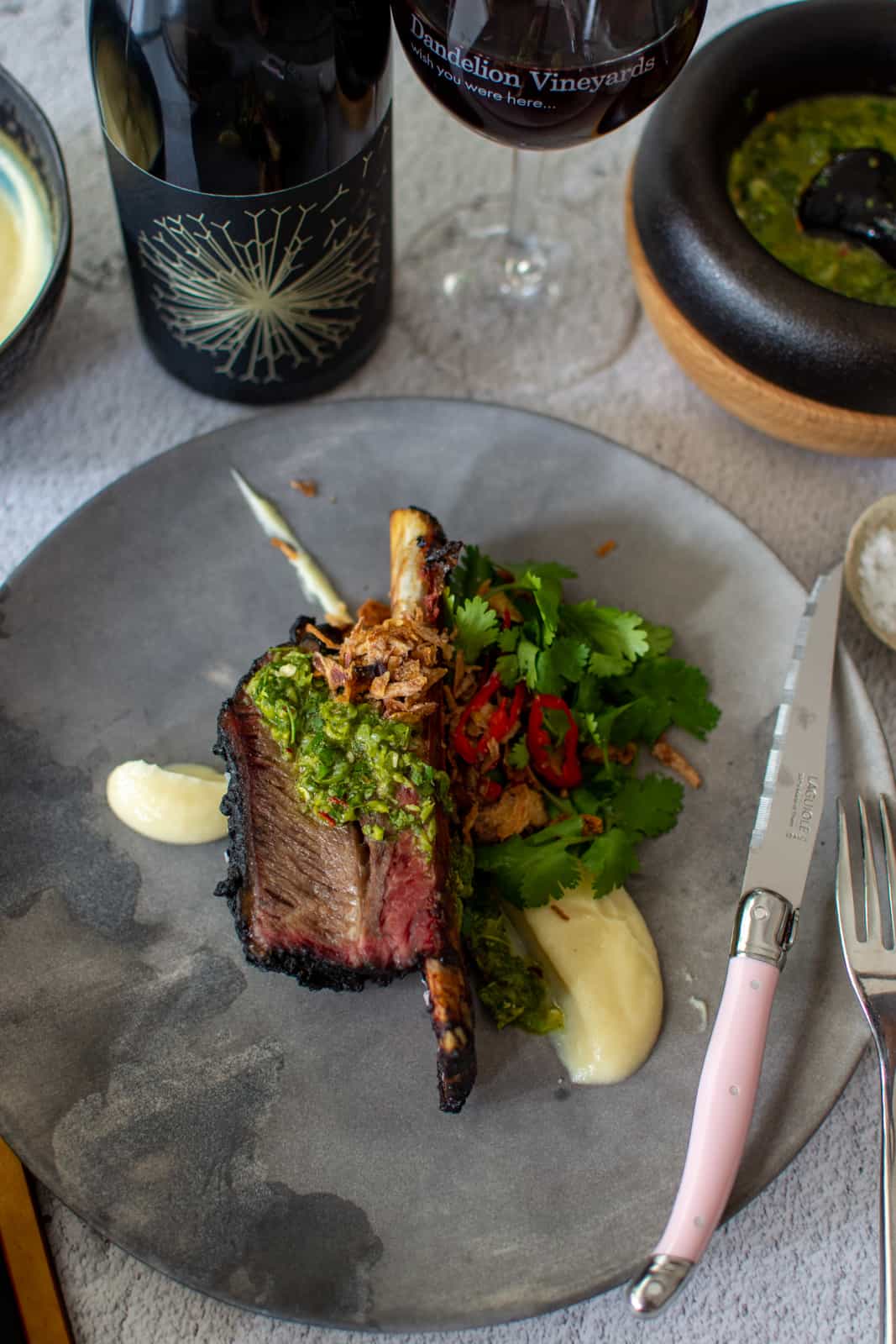 smoked short rib on a grey plate with cauliflower puree and chimichurri. A bottle of dandelion wine behind it