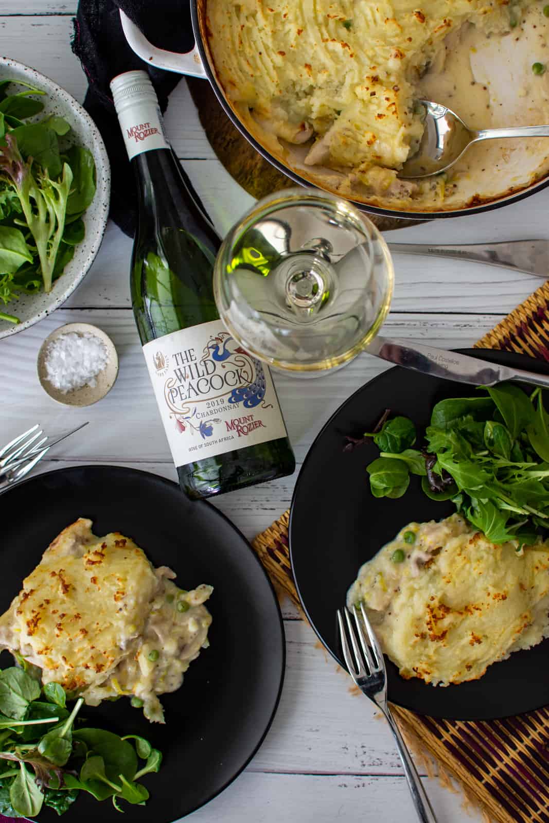 chicken and mushroom pie on plates with salad and a bottle of chardonnay next to them 