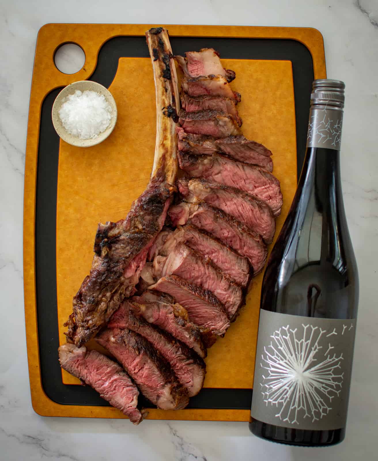 sliced grilled tomahawk steak and a bottle of wine on a chopping board