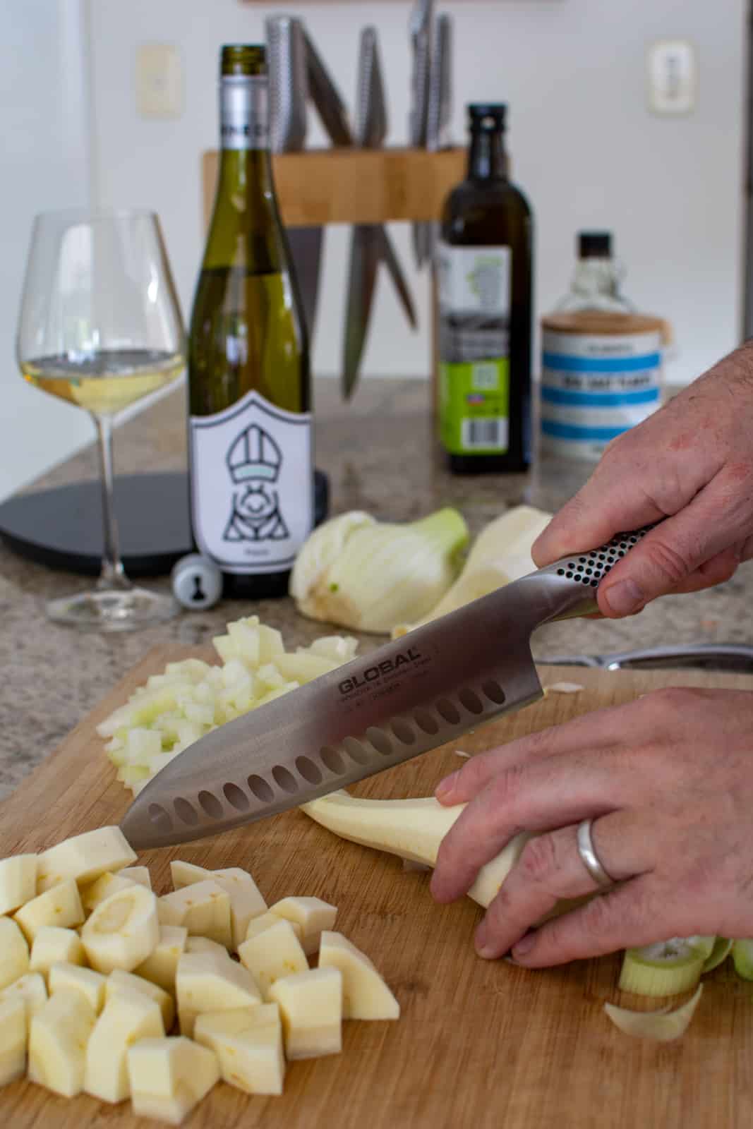 Someone cutting vegetables in a kithchen with wine & chef knives in the background