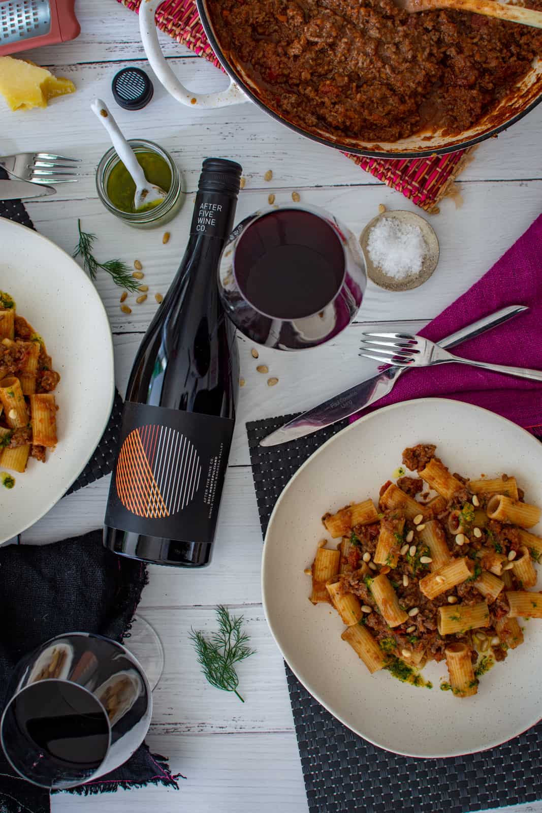 lamb mince ragu in a bowl on white table with wine, napkins, parmesan and cutlery around it