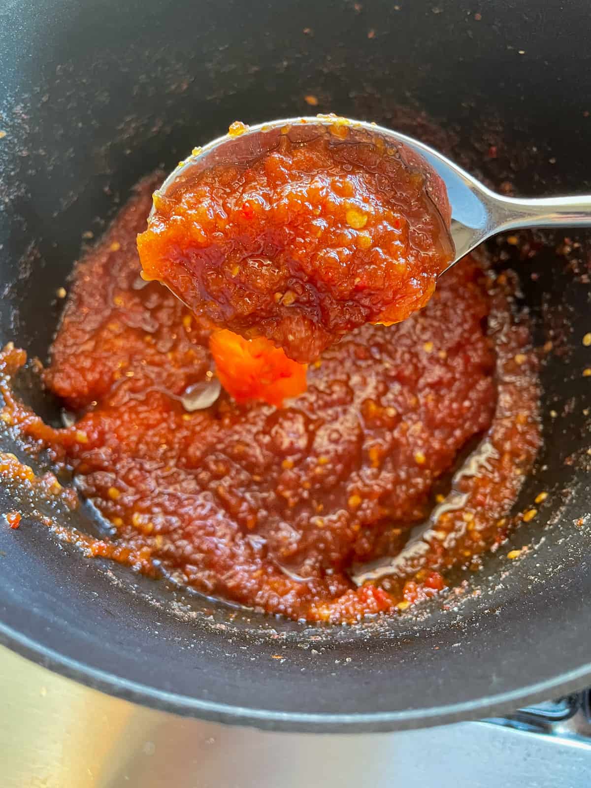 tomato chilli jam on a spoon above a saucepan