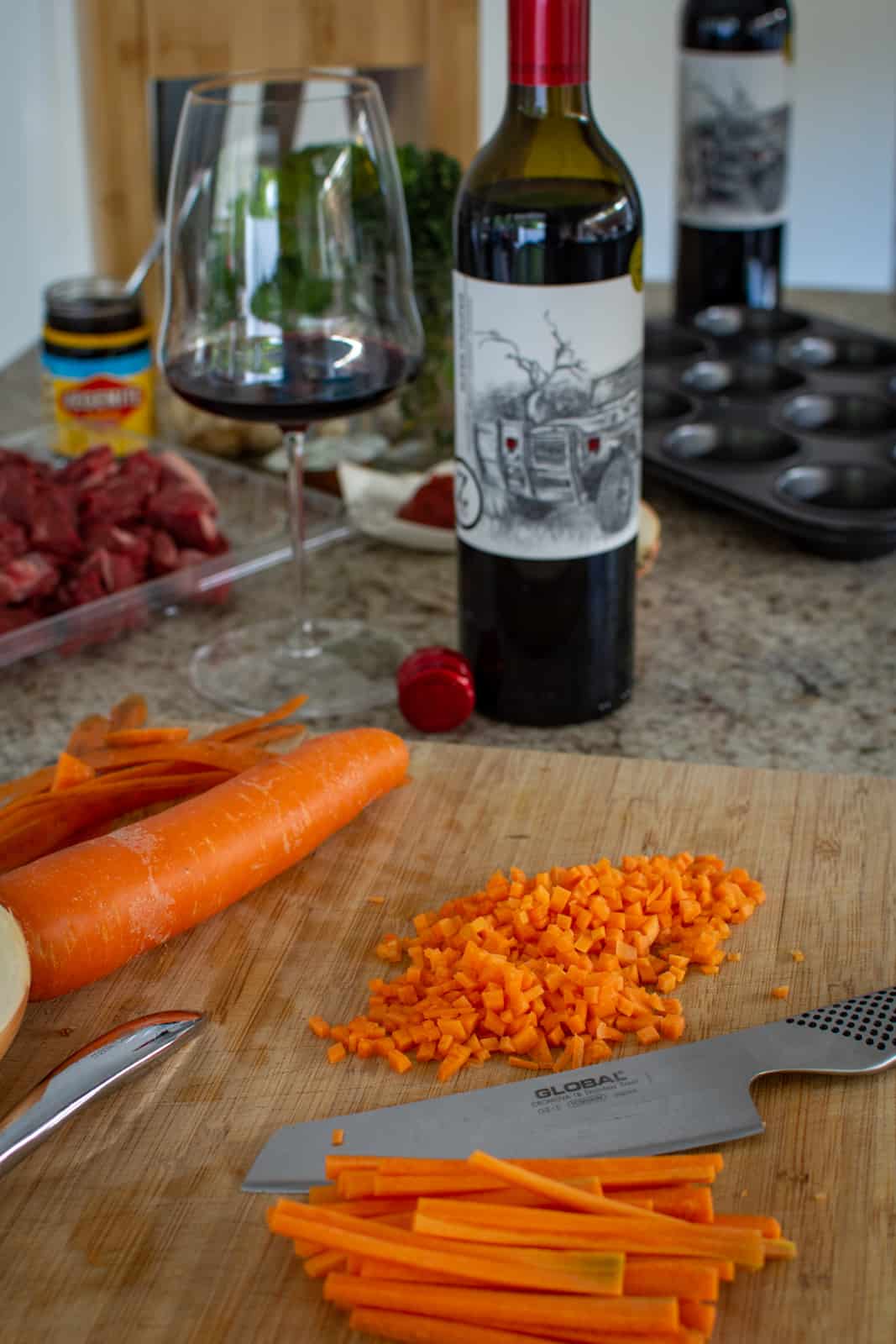 carrots being chopped on chopping board with other ingredients and wine in background