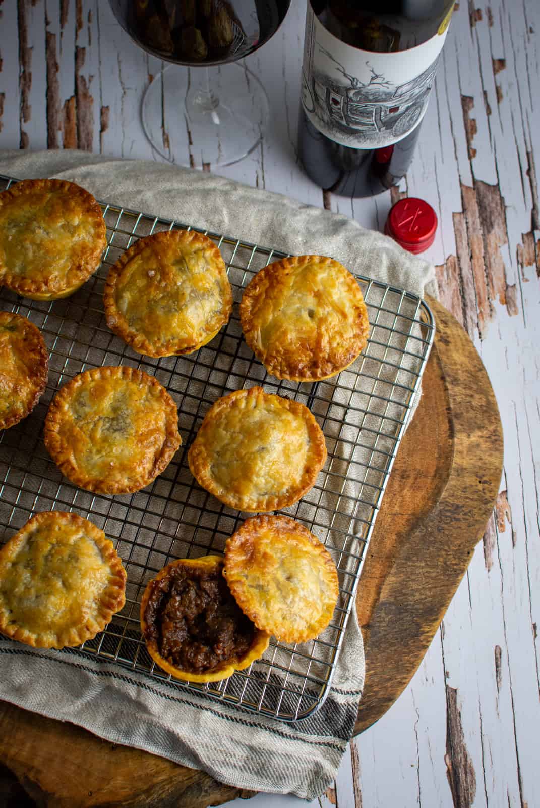 Beef pies on a wire rack with wine beside them 