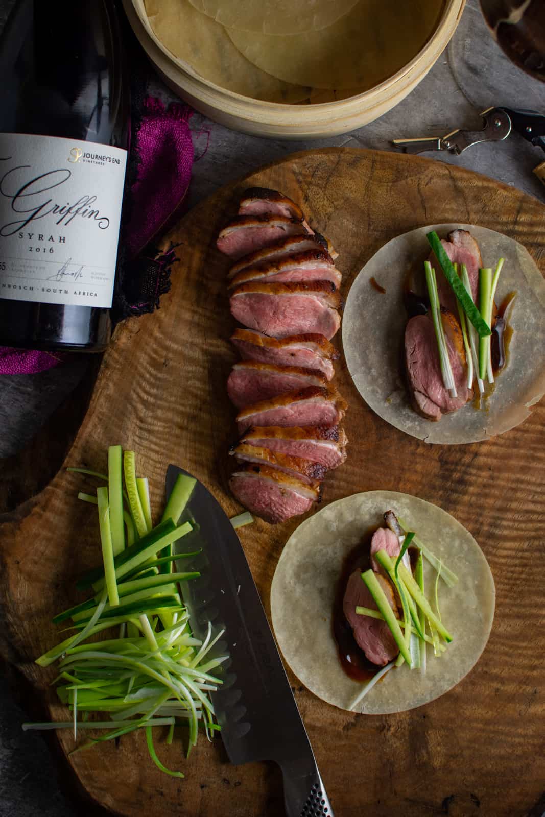 peking duck pancakes on a wooden board, duck breast and Griffin syrah next to board 