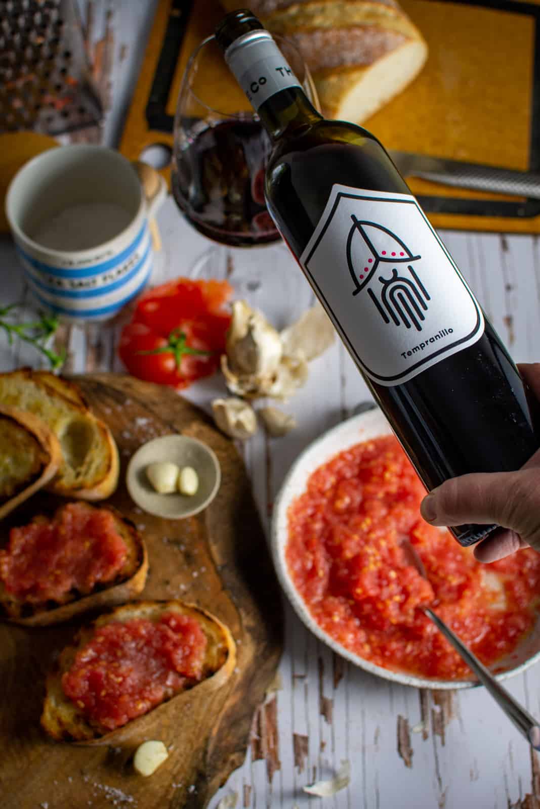 someone pouring Pawn Wine Co Tempranillo with food in the background